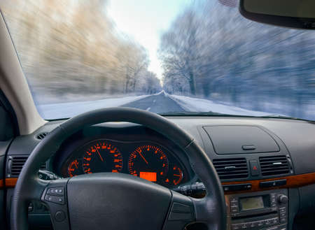 View through the car windshield on to winter road in the forest blurred in motion with dashboard and...