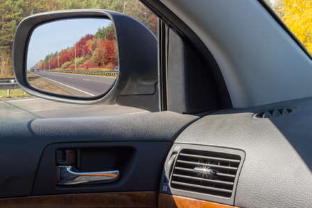 Reflected highway and roadside in the Ñar side rear-view mirror through the open side window in autumnの写真素材
