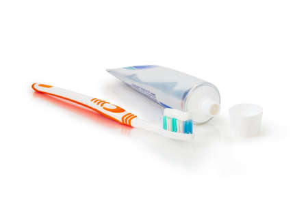 White and orange toothbrush with toothpaste and tube of toothpaste with open lid on white matte...