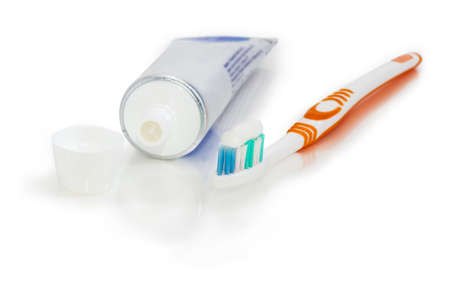 White and orange toothbrush with toothpaste and tube of toothpaste with open lid on white matte surface at shallow depth of field
の写真素材