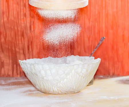 Wheat flour during sifting through a wooden sieve into a glass bowl on a table
の写真素材