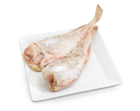 Two carcasses of the frozen red cod without heads on a large square white dish on a white...