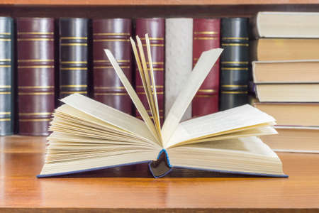 Open book with blue cover on a wooden table at selective focus with blurred text against of the other books on the background 
の写真素材