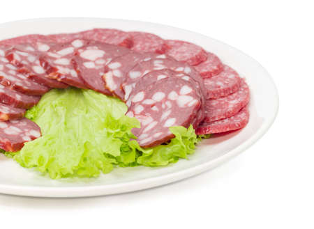 Fragment of the dish with sliced salami and smoked sausage closeup on lettuce leaf with selective focus on a white backgroundの写真素材