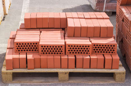 Red perforated building bricks with round holes on wooden pallet on an outdoor warehouse in sunny dayの写真素材