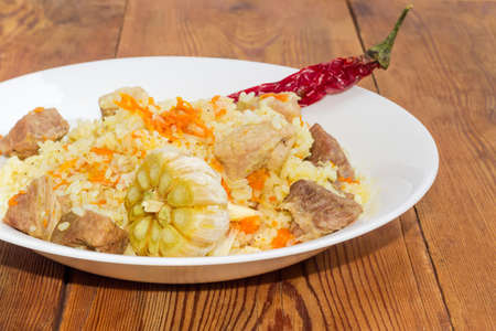 Fragment of the white dish with cooked pilaf, whole garlic head who was immersed in a dish during...