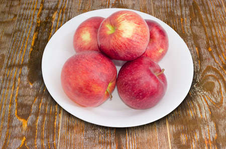 Several red ripe apples on a white dish on the old wooden rustic tableの写真素材