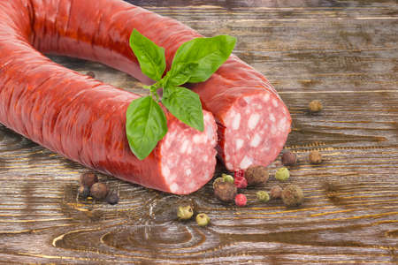 Smoked sausage in natural casing curtailed by a ring with twig of fresh basil and scattered...