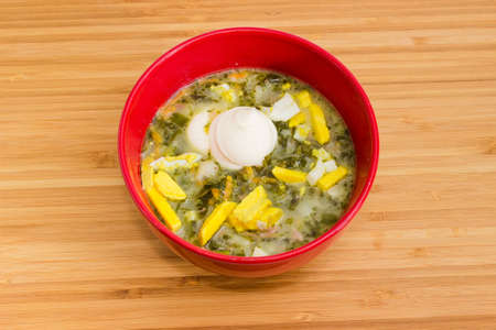Top view of sorrel soup also known as green borscht with chopped egg and sour cream in red bowl on a wooden tableの写真素材