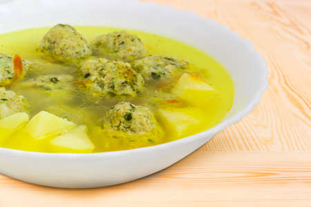 Fragment of the white bowl with chicken meatballs soup closeup on a light colored wooden surface at selective focus の写真素材