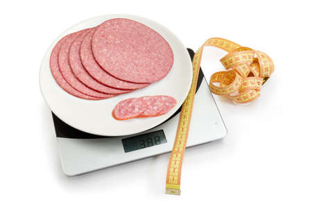 Yellow tape-line and slices of sausage different sizes on the digital kitchen scale on a white background. Concept of overeating, excess weight and obesity.の写真素材
