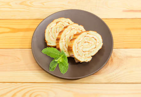 Slices of Swiss roll with buttercream and jam and sprig of mint on the brown dish on a light colored...