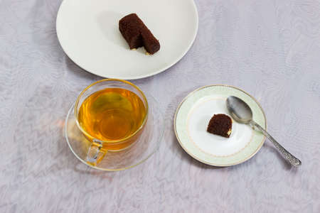 Partly sliced chocolate pastry, glass cup of tea and very small piece of pastry on saucer as concept of combating of excess weight and obesity.の写真素材