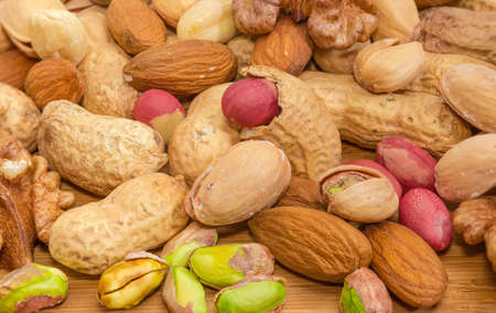 Background of pile of the different peeled nuts and nuts in their shells on a bamboo wooden surface