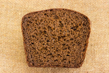 Top view of cut of brown rye and wheat bread loaf on a blurred background of sackcloth