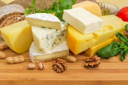 Pieces of different soft and semi-soft cheese with mold, medium-hard and hard cheese among of nuts and greens on the bamboo wooden surfaceの写真素材
