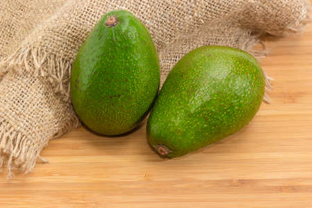 Two whole green-skinned pear-shaped avocado fruit on a wooden bamboo surface