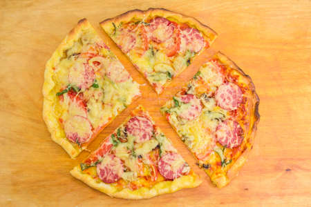 Cooked round pizza with sausages, tomatoes and mushrooms cut into four parts on a wooden cutting...