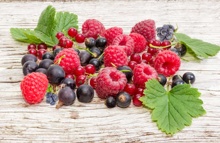 Pile of the various berries and some leaves on an old wooden plank close-up