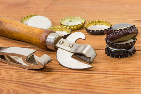 Fragment of the vintage multipurpose bottle opener and bottle opener in the form of a keychain among of different used bottle caps on the rustic table close-up at selective focusの写真素材