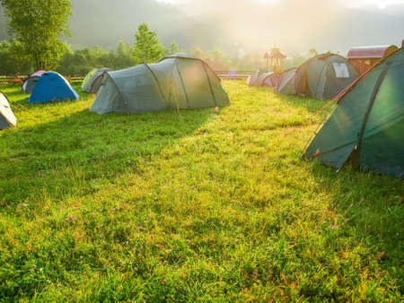 Fragment of tourist tent camp on a mountain meadow covered with grass with dew at sunriseの写真素材