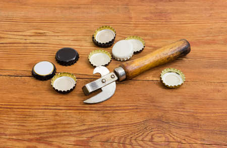 Vintage multipurpose bottle opener with wooden handle among of used different bottle caps on a...