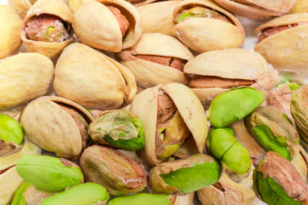 Background of the roasted salted pistachio nuts peeled from shells and nuts with partly open shells closeup at selective focusの写真素材