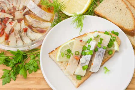 Top view of the open sandwich with slices of pickled Atlantic herring fillet, lemon and green onion...