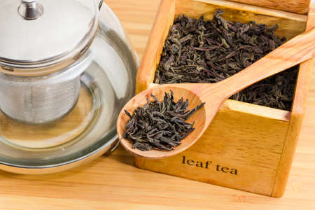 Dried large leaves of black tea in wooden spoon on background of wooden box with tea and empty glass...