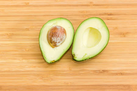 Green-skinned pear-shaped avocado fruit cut in half on bamboo cutting board