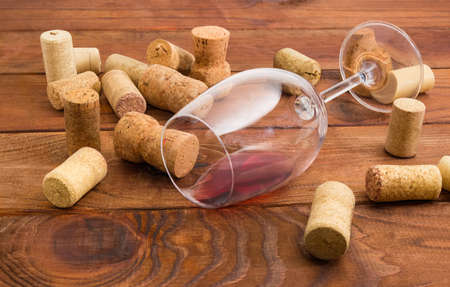 Wine glass lying on its side with small amount of red wine among of different wine corks on a dark...