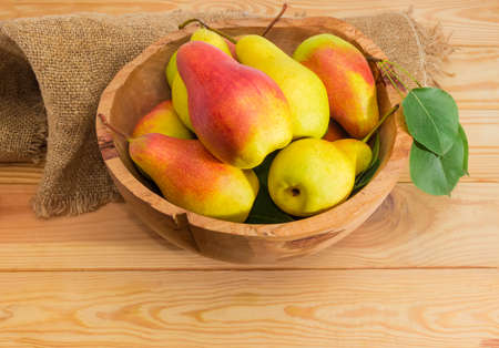 Ripe red and yellow European pears with leaves in the vintage wooden fruit bowl on sackcloth and surface of the light colored wooden planksの写真素材