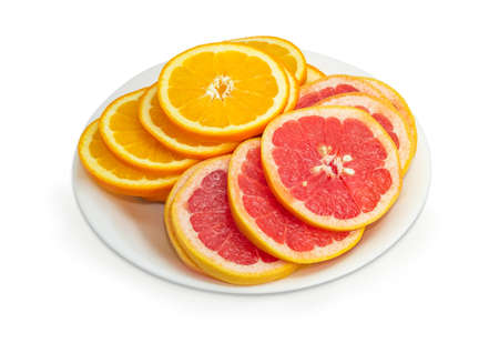 Pile of the round slices of the ripe oranges and red grapefruits with their peel on the white dish on a white backgroundの写真素材