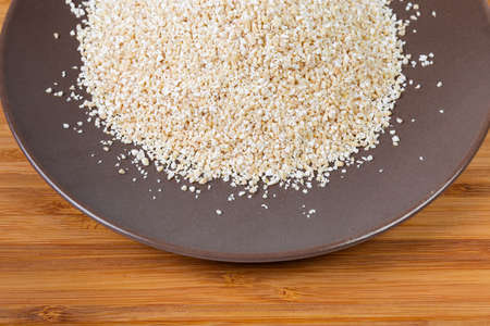 Fragment of the brown ceramic dish with raw fine-ground barley groat close-up on a bamboo wooden surfaceの写真素材