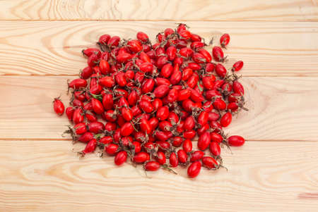 Pile of dried red fruits of the dog rose on the light-colored wooden rustic table