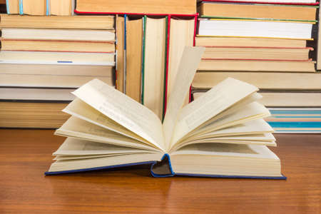 Open book with blurred text in blue hardcover on a wooden table against of the other stacked up books on the backgroundの写真素材