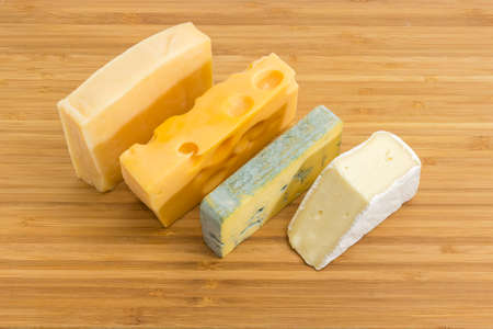 Pieces of blue cheese, brie, medium-hard Swiss and hard cheese on the bamboo cutting board