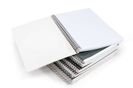Open blank exercise book with pages of squared paper and wire spiral binding on stack of other exercise books on a white backgroundの写真素材
