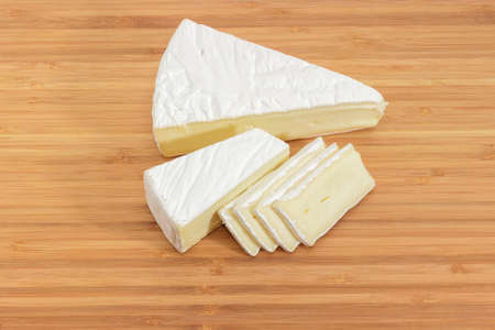 Pieces and slices of the brie cheese on a bamboo wooden cutting board