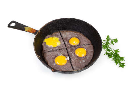 Fried eggs sunny side up prepared by beating egg white with black olives and unbroken yolks on old cast iron frying pan and parsley on a white backgroundの写真素材
