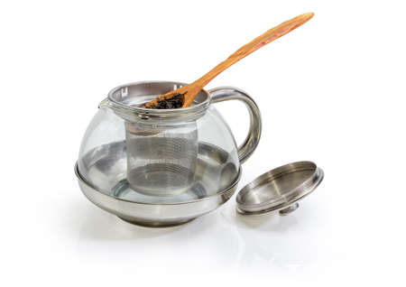 Dried large leaves of black tea in wooden spoon on eEmpty glass teapot with strainer and open lid on a white backgroundの写真素材