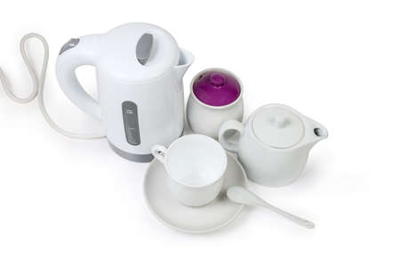 Small white electric kettle, teapot, sugar bowl and empty cup with ceramic tea spoon on saucer on a white backgroundの写真素材