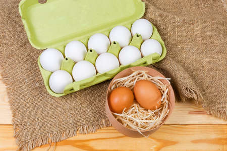 Top view of the brown and white chicken eggs in round wooden box and open egg carton made of...