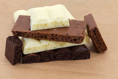 Pieces of the dark, milk and white aerated chocolate close-up on a wrapping-paper at selective focus