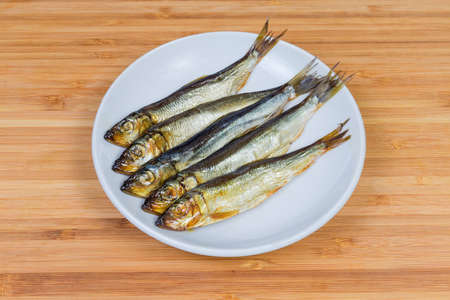 Smoked baltic herring on the white saucer on a bamboo wooden surfaceの写真素材