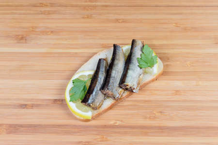 Open sandwich with smoked sprats preserved in vegetable oil and lemon slices on a bamboo wooden cutting boardの写真素材