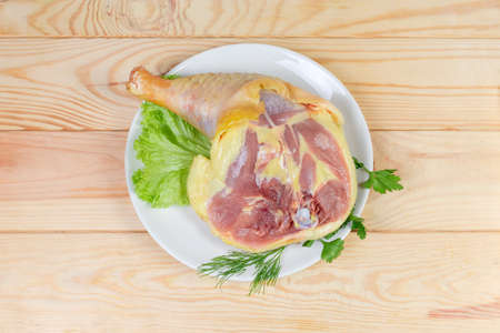 Top view of the raw leg quarter of broiler Ñhicken reared by free range method outdoors and having a characteristic yellowish skin, greens on dish on a light colored rustic wooden tableの写真素材
