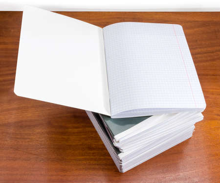 Open blank exercise book with pages of squared paper and red vertical lines for a margins on stack of other exercise books on the wooden tableの写真素材
