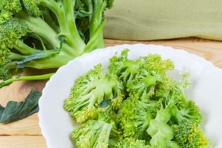 Fragment of white dish with pieces of the fresh broccoli against of broccoli head close-up on wooden surfaceの写真素材