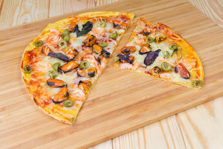Partly slised round pizza with seafoods and olives on a bamboo cutting board on the wooden rustic tableの写真素材